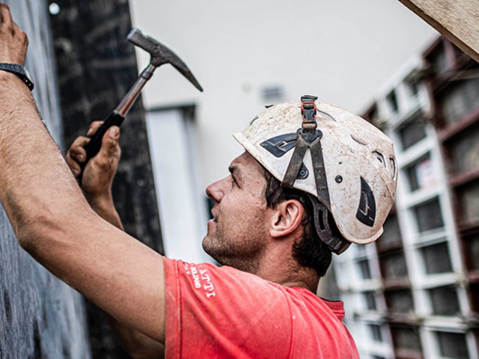 Südtirols Baubranche: „Uns steht die Krise noch bevor“ Bauarbeiter mit Helm hämmert an Wand bei Baustelle