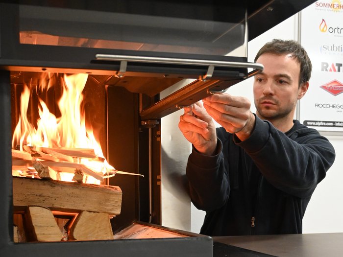 Sicher durch die Heizsaison Mann zündet Holzscheite in einem Ofen an