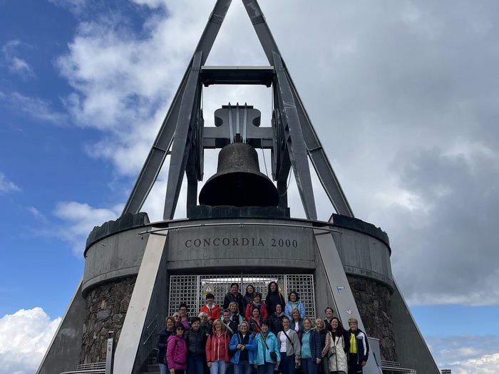 Unternehmerfrauen im Pustertal Gruppe vor der Concordia 2000 Glocke auf einem Berg unter bewölktem Himmel