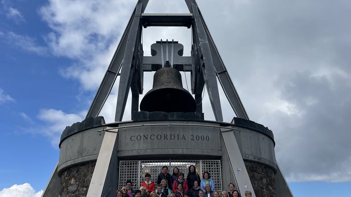 Unternehmerfrauen im Pustertal Gruppe vor der Concordia 2000 Glocke auf einem Berg unter bewölktem Himmel