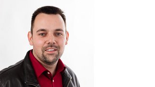 News Porträt eines lächelnden Mannes mit rotem Hemd und schwarzer Lederjacke vor weißem Hintergrund