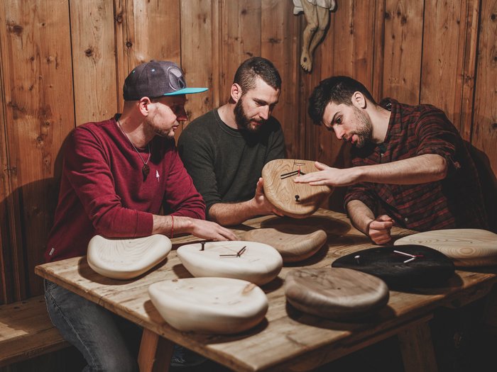 Drei Unternehmer am Tüfteln – Foto: © huamet Drei Männer besprechen handgefertigte Holzuhren an einem Holztisch