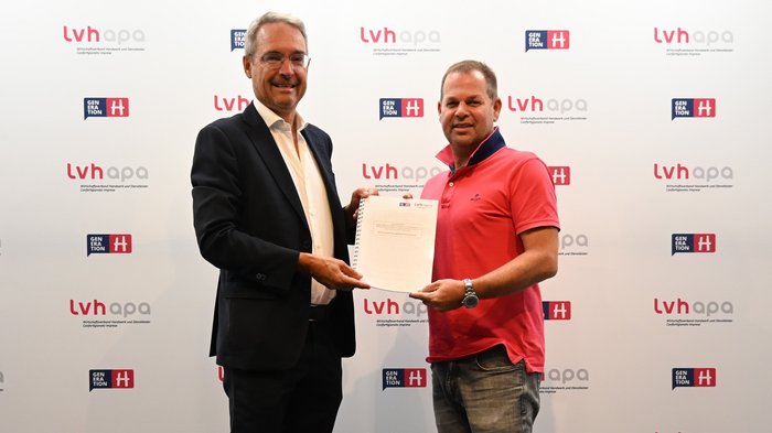 Dieter Steger im Haus des Handwerks Zwei Männer halten gemeinsam ein Dokument vor einer LVHAPA-Wand