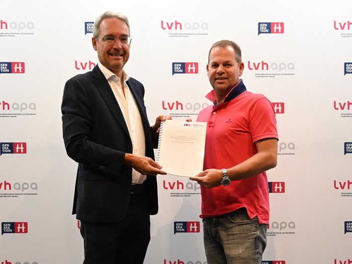 Dieter Steger im Haus des Handwerks Zwei Männer halten gemeinsam ein Dokument vor einer LVHAPA-Wand