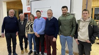 News Sieben Personen stehen vor einem Rednerpult und Banner in Innenraum