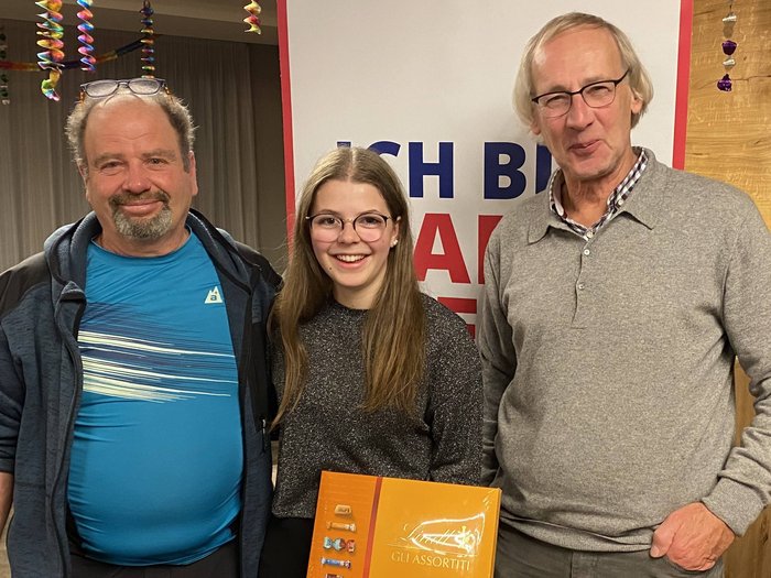 Schlanders: Glückwünsche und viele Aktivitäten Drei lächelnde Personen, junge Frau hält Lindt Schokoladenbox