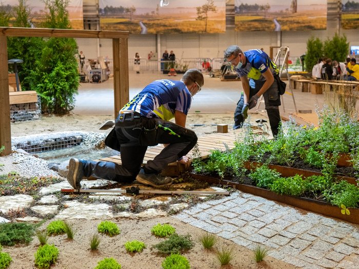 Oro e medaglia d'eccellenza per l'Alto Adige Due uomini curano un giardino con piante e passerella in legno in un capannone