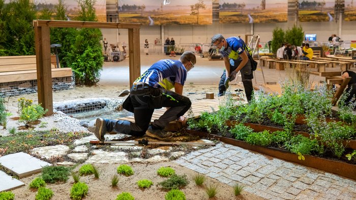 Gold und Medaillon for Excellence für Südtirol Zwei Männer gestalten eine Gartenanlage mit Pflanzen und Holzbelag in einer Halle