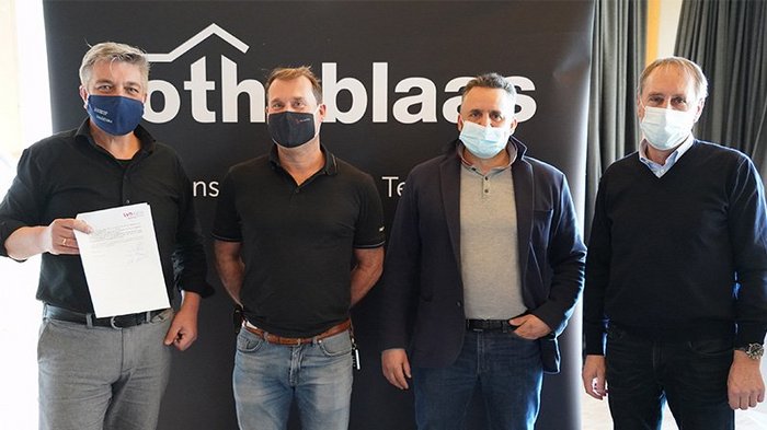 Holzbau in Südtirol: Neue Kooperation im Zeichen der Innovation Vier Männer mit Gesichtsmasken vor Firmenbanner, einer hält ein Dokument