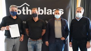 News Vier Männer mit Gesichtsmasken vor Firmenbanner, einer hält ein Dokument