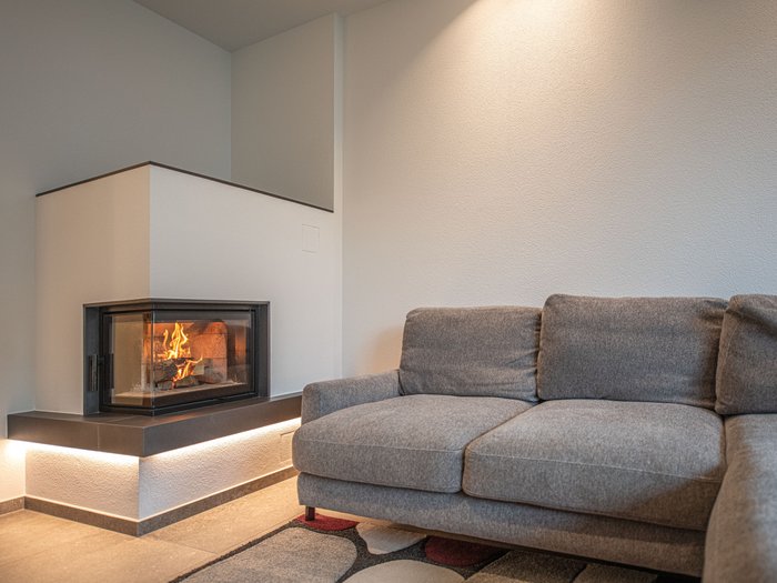Information und Prävention Moderner Wohnzimmerbereich mit grauem Sofa und eingebautem Kamin mit Feuer