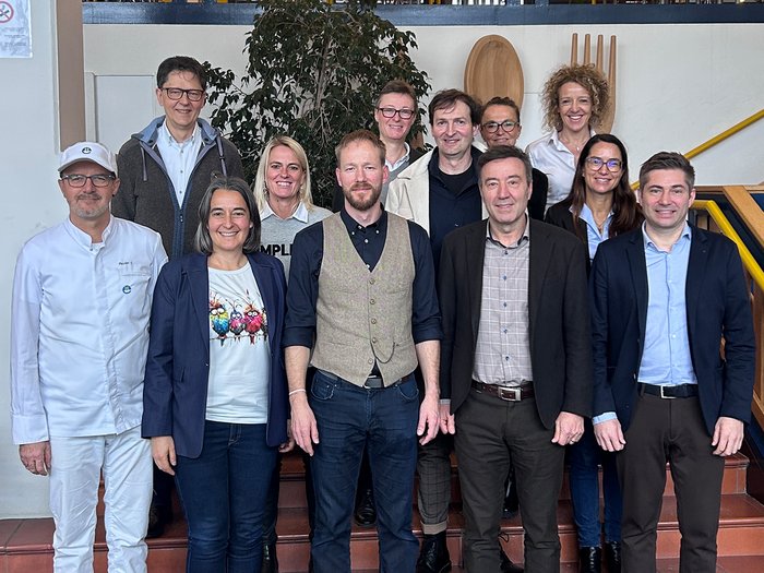 lvh zu Besuch im Berufsbildungszentrum „Emma Hellenstainer“ Gruppenfoto von zwölf Personen in Innenraum vor Treppe und Wanddekoration