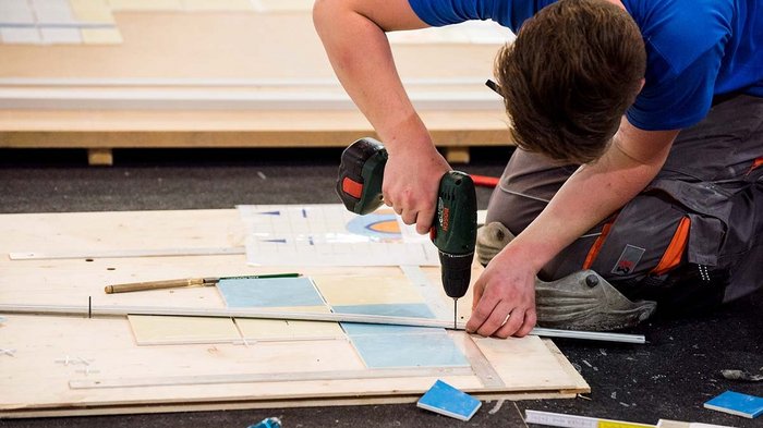 Wiedereröffnung der handwerklichen Tätigkeiten und der kleinen Arbeitsstätten und Baustellen Handwerker bohrt Löcher in Holzplatte für Fliesenverlegung