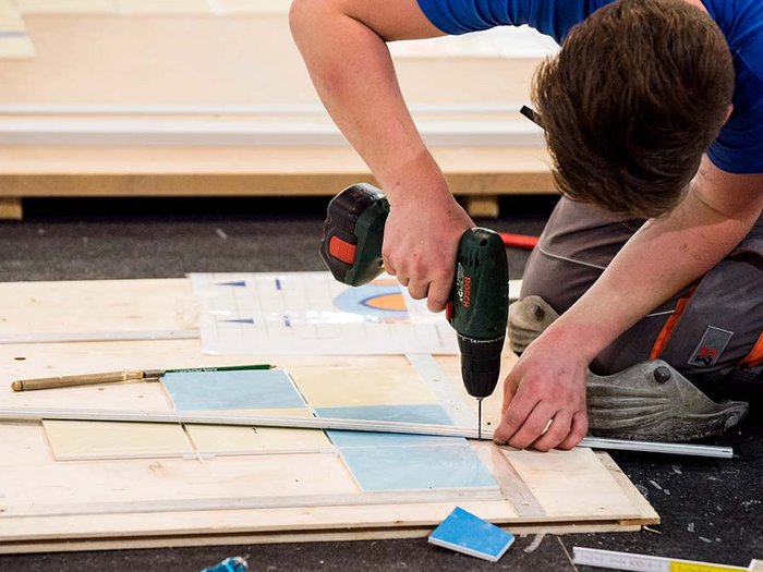 Wiedereröffnung der handwerklichen Tätigkeiten und der kleinen Arbeitsstätten und Baustellen Handwerker bohrt Löcher in Holzplatte für Fliesenverlegung