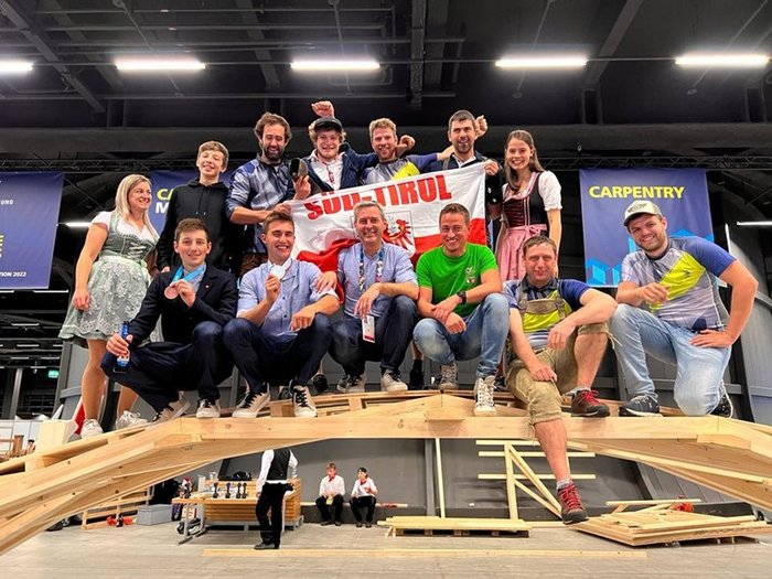 WorldSkills 2022 Special Edition: Zimmerer Marcel Bolego holt Silbermedaille Gruppenfoto von Personen auf einer Holzkonstruktion mit Südtirol-Flagge bei Zimmermannswettbewerb