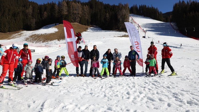 Südtirols erster Handwerker-Snowpark eingeweiht Kinder und Skilehrer posieren auf einer Piste mit zwei Fahnen und Schnee im Hintergrund