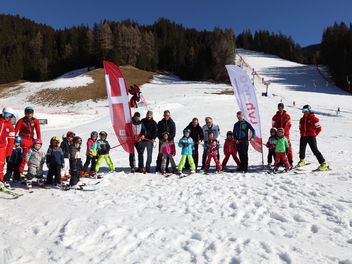 Südtirols erster Handwerker-Snowpark eingeweiht Kinder und Skilehrer posieren auf einer Piste mit zwei Fahnen und Schnee im Hintergrund