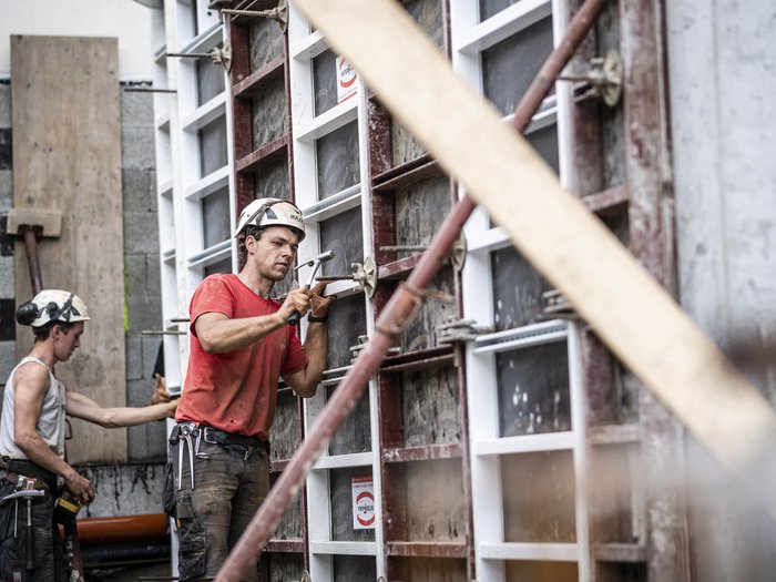 © Hannes Niederkofler Bauarbeiter mit Helm arbeiten an Schalung auf Baustelle