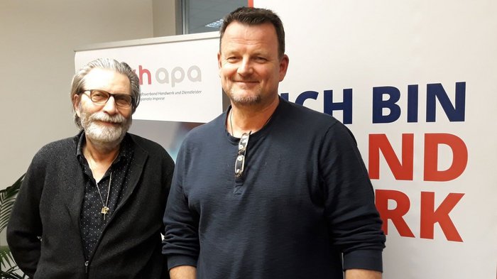 Pfanzelter bleibt Obmann der Glaser/innen Zwei Männer stehen vor einem Banner mit Text und lächeln in die Kamera.