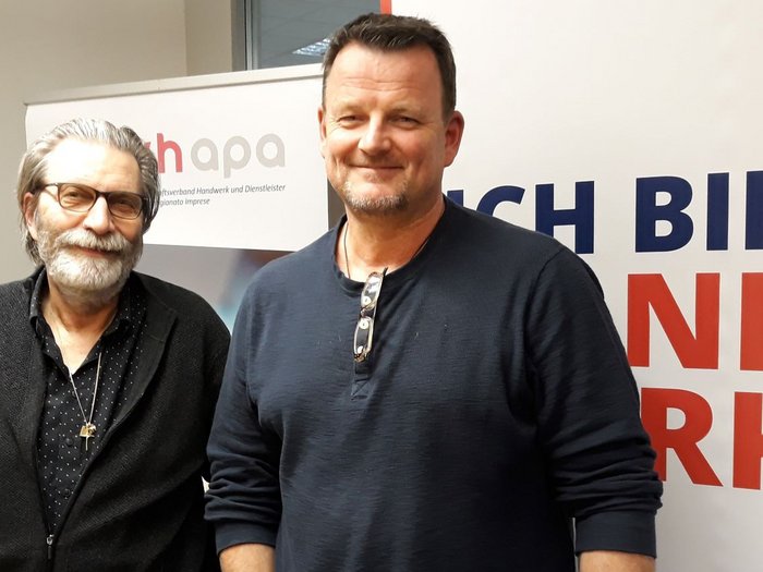 Pfanzelter bleibt Obmann der Glaser/innen Zwei Männer stehen vor einem Banner mit Text und lächeln in die Kamera.