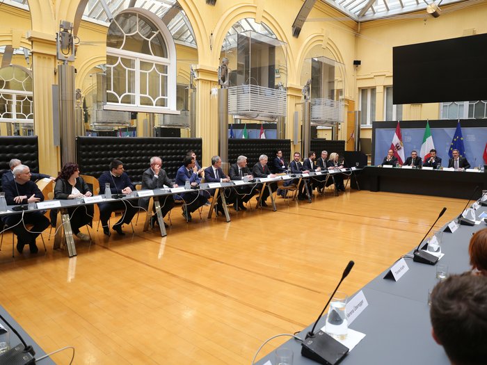 Brenner - Handelskammern von Bozen und Trient sowie die Transportverbände: Die Tiroler Fahrverbote sind längst überholt Große Sitzung mit mehreren Teilnehmern in einem Konferenzraum mit Fahnen