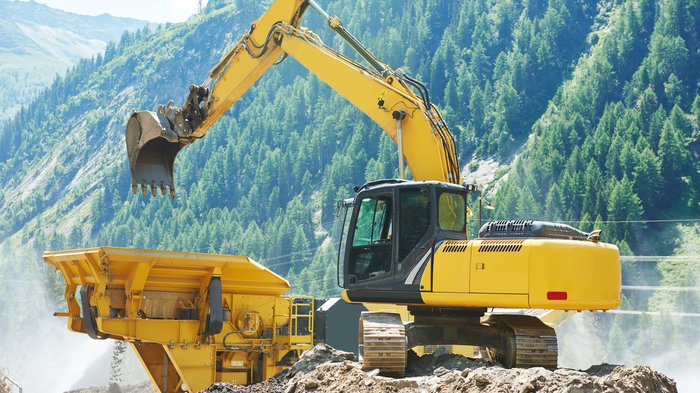 Gemeinsame Linie Gelber Bagger belädt eine Maschine vor bewaldeten Bergen