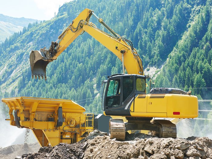 Gemeinsame Linie Gelber Bagger belädt eine Maschine vor bewaldeten Bergen