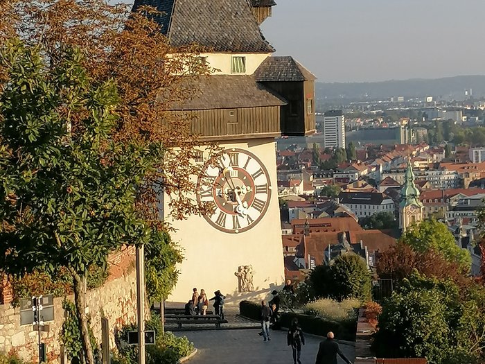 Unsere Althandwerker zu Besuch in der Stiermark Uhrturm mit Stadtblick und Menschen auf einem Gehweg in Graz