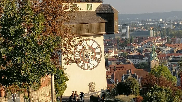 Unsere Althandwerker zu Besuch in der Stiermark Uhrturm mit Stadtblick und Menschen auf einem Gehweg in Graz