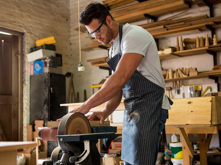 Falegnami Uomo che leviga il legno in una bottega con occhiali di protezione e grembiule