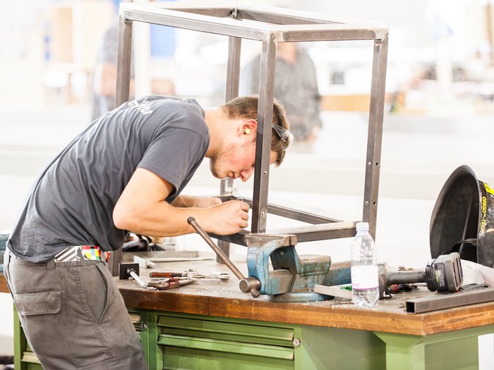Le parti sociali rafforzano l'artigianato confermando i contratti integrativi territoriali Uomo lavora su struttura metallica su banco da lavoro con utensili e casco