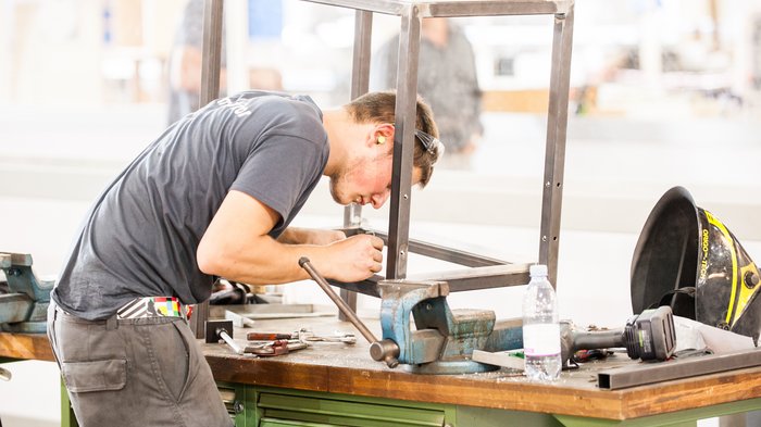 Sozialpartner stärken Handwerk durch Bestätigung territorialer Zusatzverträge Mann fertigt Metallrahmen auf Werkbank mit Werkzeugen und Schutzhelm