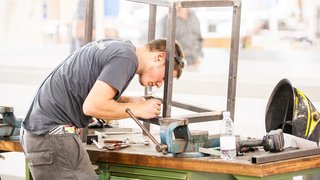 News Mann fertigt Metallrahmen auf Werkbank mit Werkzeugen und Schutzhelm