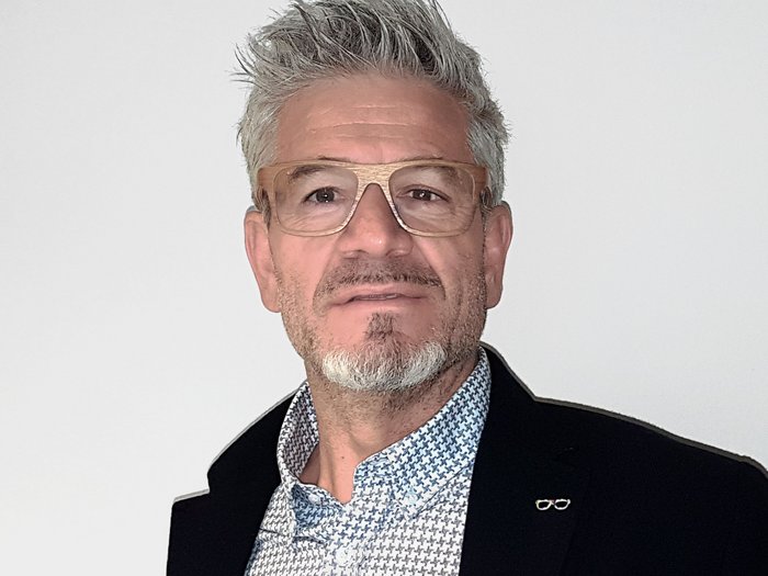 Lohnausgleich sorgt für Unmut in Baubranche Mann mit grauen Haaren, Holzbrille und gemustertem Hemd vor weißem Hintergrund