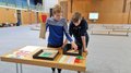 Schulprojekt "Clever gebaut": Selbst entwickelte Spiele prämiert Zwei Jungen spielen an einem Tisch mit bunten Spielmaterialien in einer Turnhalle