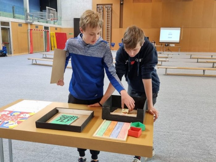 Schulprojekt "Clever gebaut": Selbst entwickelte Spiele prämiert Zwei Jungen spielen an einem Tisch mit bunten Spielmaterialien in einer Turnhalle