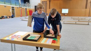 News Zwei Jungen spielen an einem Tisch mit bunten Spielmaterialien in einer Turnhalle