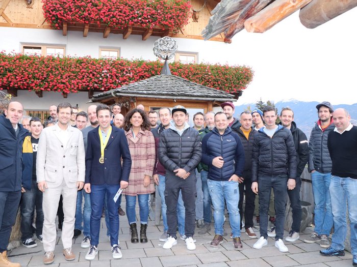 KFZ-Mechatroniker feiern ihren Weltmeister Gruppenfoto vor einem Haus mit Blumen und Bergen im Hintergrund