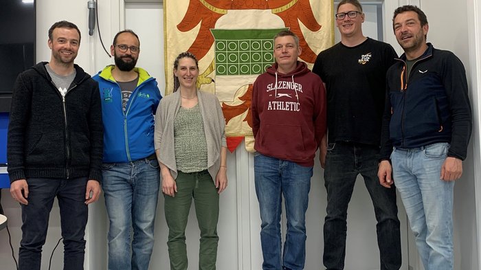 Engagiert für die Zukunft des Ofenbau-Handwerks Sechs Personen stehen vor einem Wappen mit Adler in einem Raum