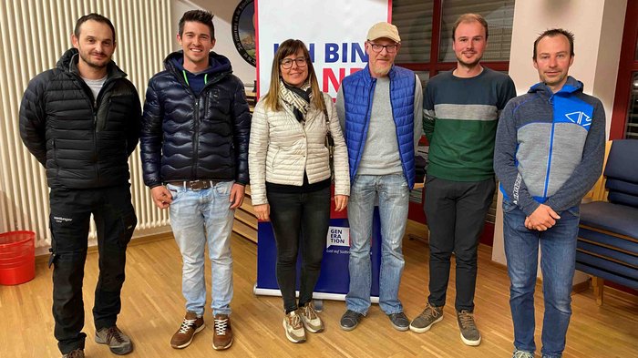 Langjähriger Ortsobmann tritt ab Sechs Personen vor einem Banner in einem Raum mit Holzboden und Stühlen