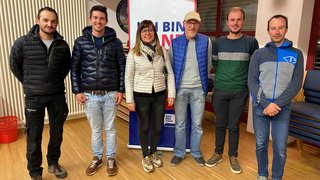 News Sechs Personen vor einem Banner in einem Raum mit Holzboden und Stühlen