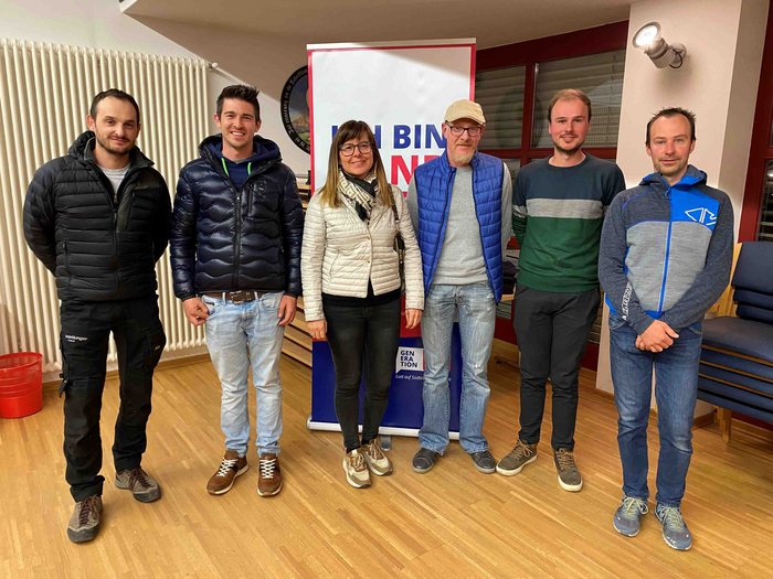 Langjähriger Ortsobmann tritt ab Sechs Personen vor einem Banner in einem Raum mit Holzboden und Stühlen