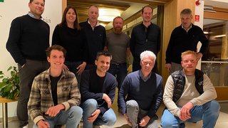 News Gruppenfoto von zehn Personen in einem Innenraum mit Holzrahmen und Pflanzen