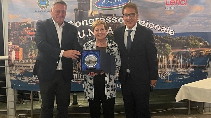 Wiederwahl einer Symbolfigur des Südtiroler Handwerks Drei Personen bei Preisverleihung vor Banner mit Hafenansicht von Lerici