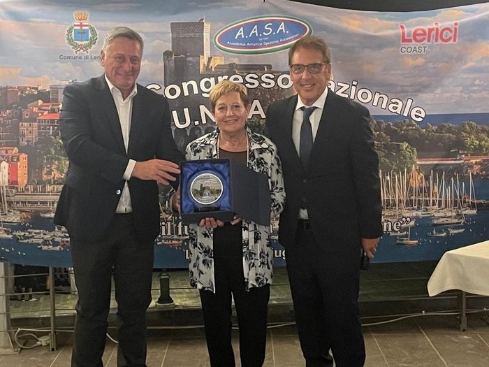 Alla guida degli acconciatori una figura simbolo dell’artigianato altoatesino Tre persone durante la premiazione davanti a uno striscione con veduta del porto di Lerici