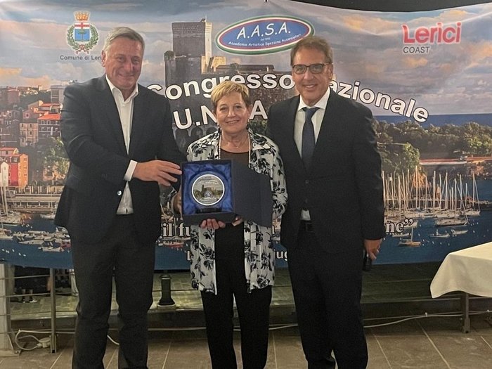 Wiederwahl einer Symbolfigur des Südtiroler Handwerks Drei Personen bei Preisverleihung vor Banner mit Hafenansicht von Lerici