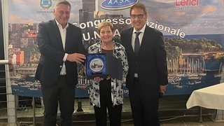 News Drei Personen bei Preisverleihung vor Banner mit Hafenansicht von Lerici