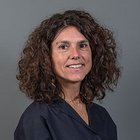 Kfz-Mechatroniker Frau mit lockigem braunem Haar vor grauem Hintergrund