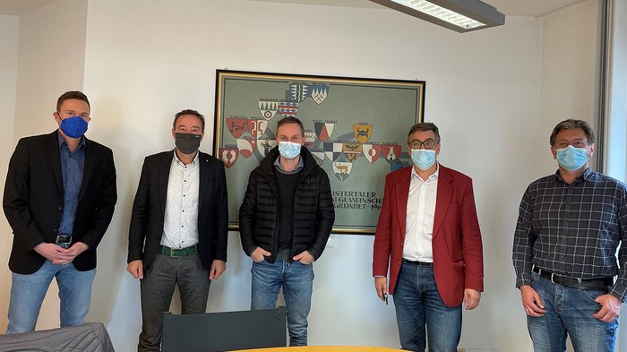 Handwerk und Bezirksgemeinschaft Pustertal wollen Zusammenarbeit verstärken Fünf Männer mit Masken stehen vor einer Wand mit Wappen in einem Besprechungsraum