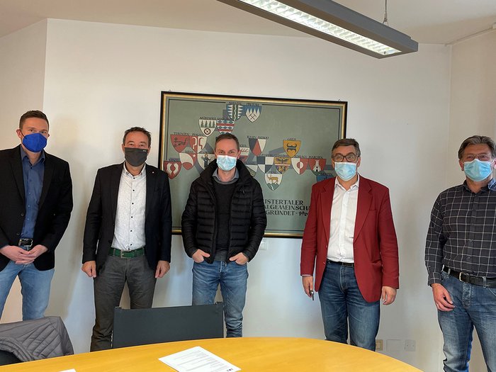 Handwerk und Bezirksgemeinschaft Pustertal wollen Zusammenarbeit verstärken Fünf Männer mit Masken stehen vor einer Wand mit Wappen in einem Besprechungsraum